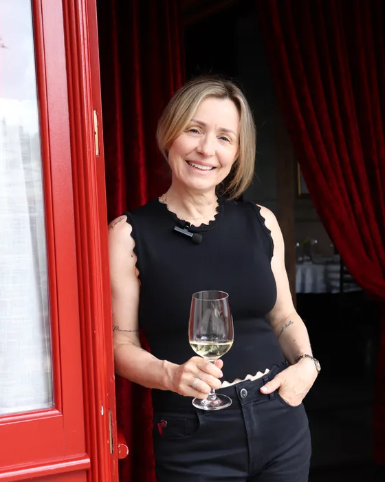 Fanie Delatte, fundadora do L'Épicerie, na porta vermelha do bistrô com uma taça de vinho