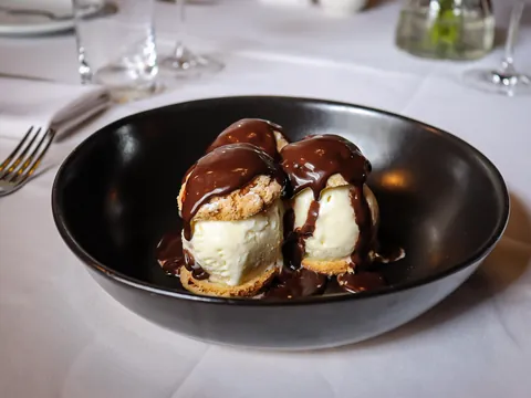 Profiteroles com sorvete e calda quente de chocolate servidos em cumbuca escura